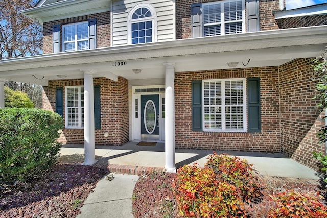 doorway to property with covered porch and brick siding