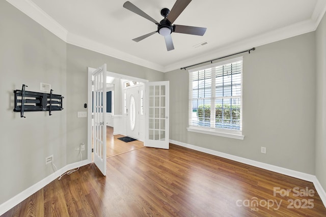 empty room featuring visible vents, crown molding, baseboards, and wood finished floors