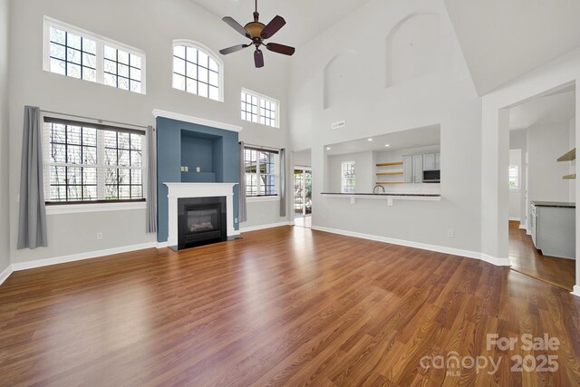 unfurnished living room featuring visible vents, a fireplace with flush hearth, dark wood finished floors, baseboards, and ceiling fan