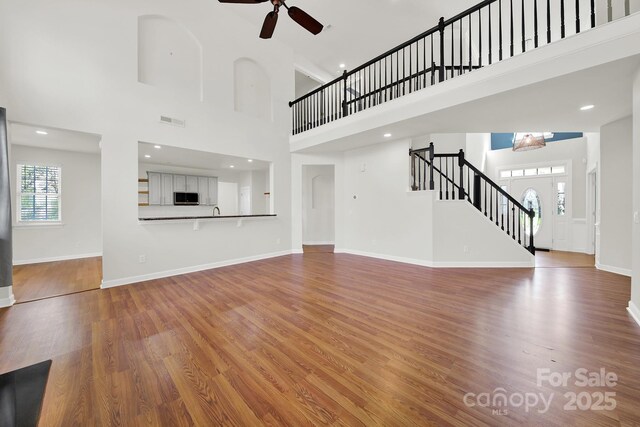 unfurnished living room with visible vents, stairs, baseboards, and wood finished floors