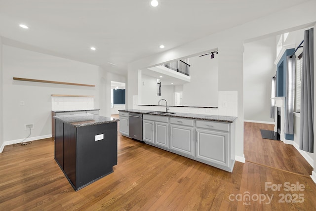 kitchen with wood finished floors, stone counters, a kitchen island, a sink, and stainless steel dishwasher