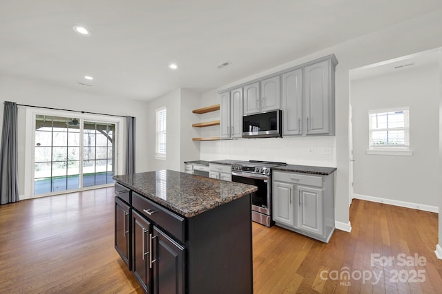 kitchen with backsplash, a center island, appliances with stainless steel finishes, light wood-style floors, and open shelves