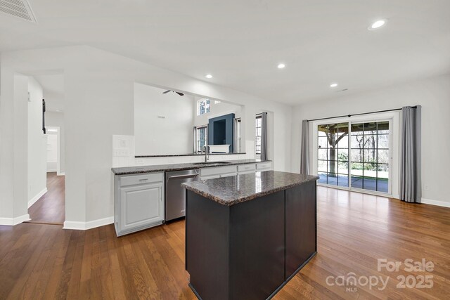 kitchen featuring visible vents, a kitchen island, dark wood-type flooring, stainless steel dishwasher, and a sink