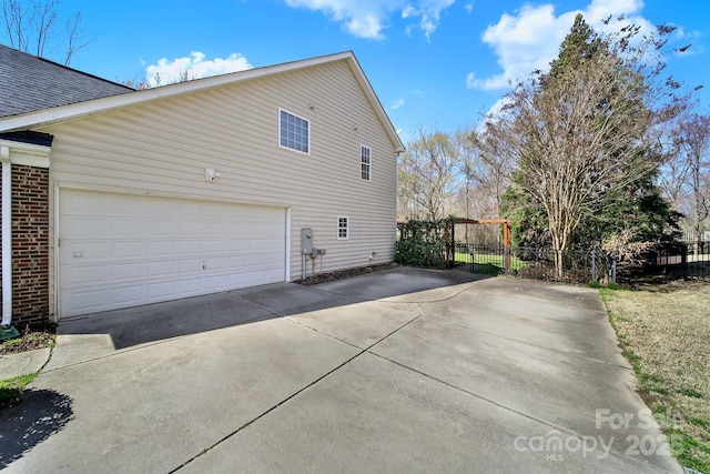 view of home's exterior featuring concrete driveway, a garage, fence, and brick siding