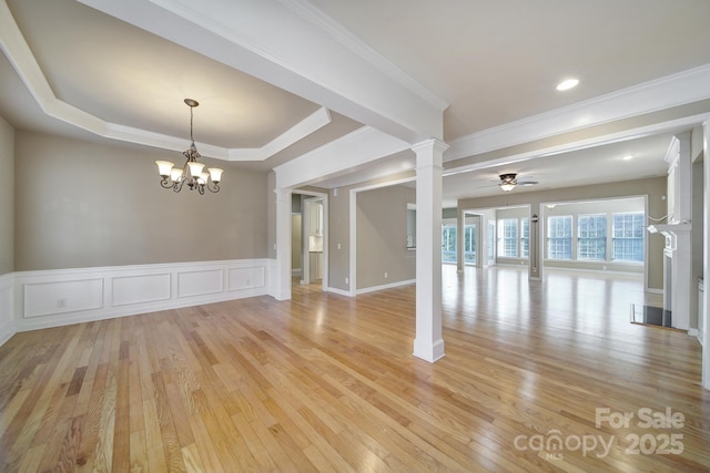 unfurnished room with light wood-style floors, wainscoting, ornate columns, and ceiling fan with notable chandelier