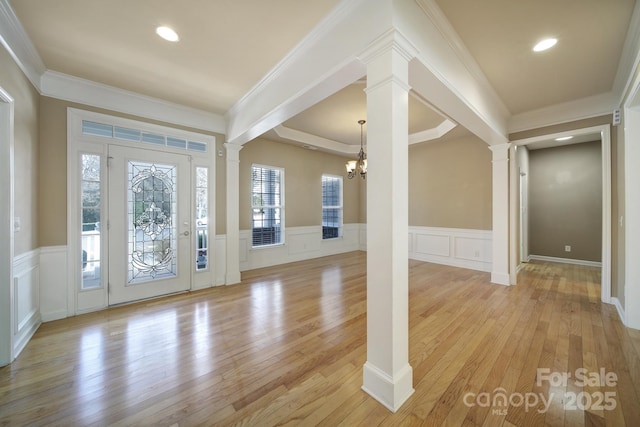 foyer with decorative columns, light wood-style flooring, an inviting chandelier, ornamental molding, and wainscoting