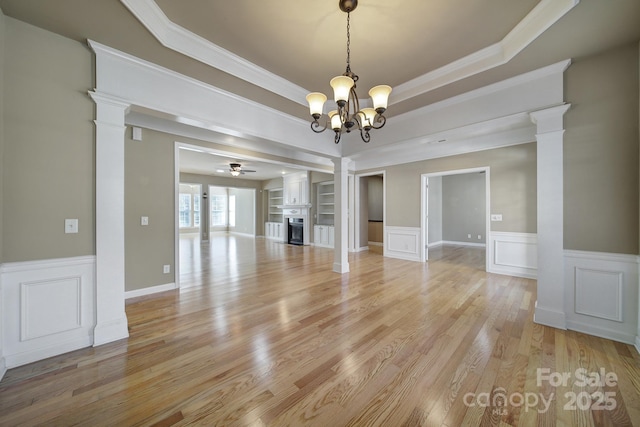 interior space featuring light wood-type flooring, a tray ceiling, a fireplace, and decorative columns