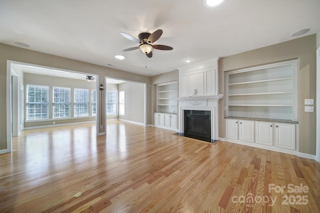 unfurnished living room with baseboards, built in features, a ceiling fan, light wood-type flooring, and a fireplace