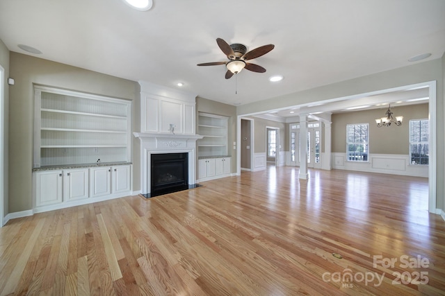 unfurnished living room with a fireplace with flush hearth, light wood finished floors, built in shelves, and ceiling fan with notable chandelier