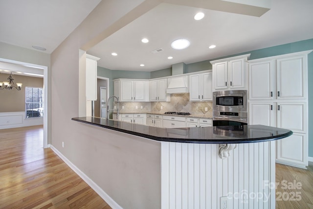 kitchen with light wood-style flooring, stainless steel appliances, a peninsula, white cabinetry, and tasteful backsplash