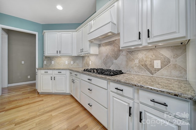 kitchen with light stone counters, gas stovetop, white cabinetry, light wood-style floors, and backsplash