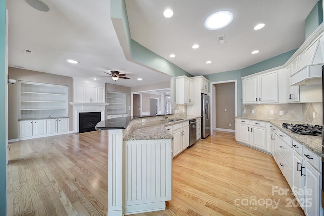 kitchen featuring a large fireplace, white cabinets, a peninsula, stainless steel appliances, and a sink