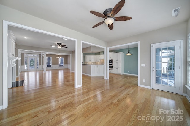 unfurnished living room with a fireplace, light wood finished floors, visible vents, ceiling fan, and baseboards