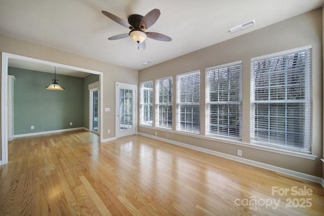 spare room featuring light wood-style flooring, a ceiling fan, visible vents, and baseboards