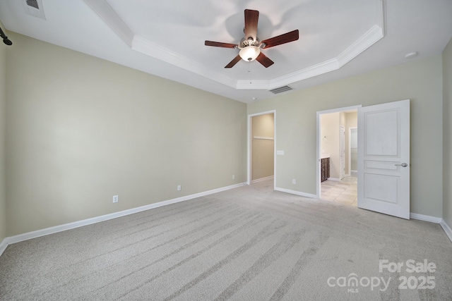 unfurnished bedroom featuring visible vents, baseboards, light colored carpet, a tray ceiling, and a walk in closet