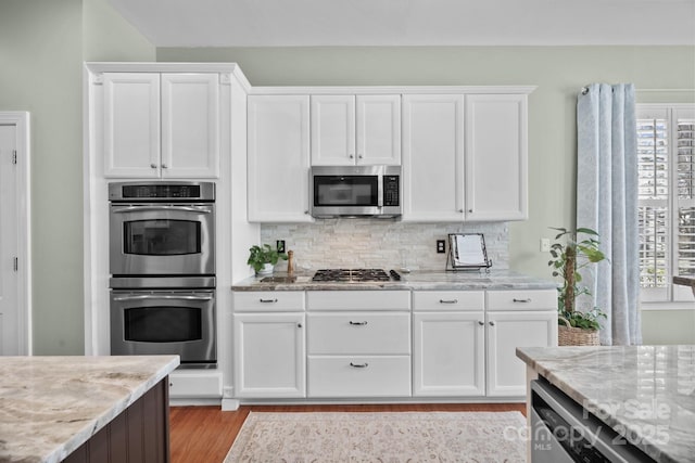 kitchen with stainless steel appliances, light wood-style flooring, decorative backsplash, white cabinetry, and light stone countertops