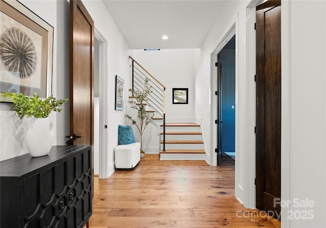 hallway with stairs, light wood-type flooring, baseboards, and recessed lighting