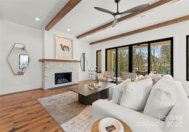 living area featuring visible vents, baseboards, a brick fireplace, hardwood / wood-style floors, and beamed ceiling