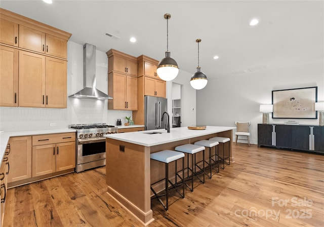 kitchen featuring a sink, light wood finished floors, wall chimney exhaust hood, and premium appliances