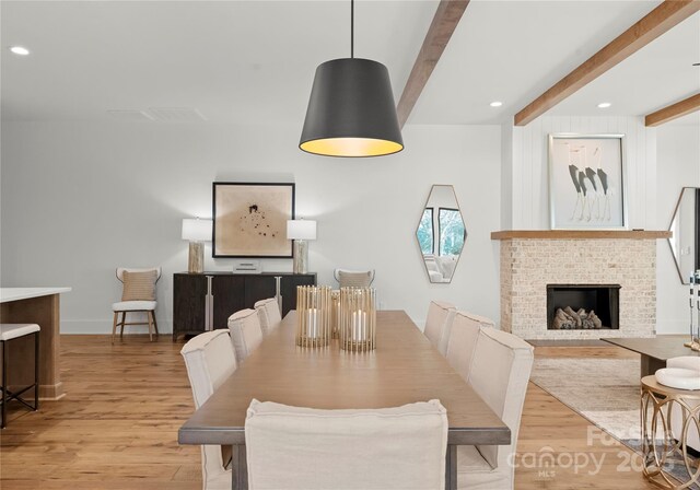 dining space featuring light wood-type flooring, a brick fireplace, beam ceiling, and recessed lighting