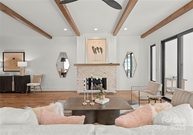 living room featuring a fireplace, beamed ceiling, baseboards, and wood finished floors