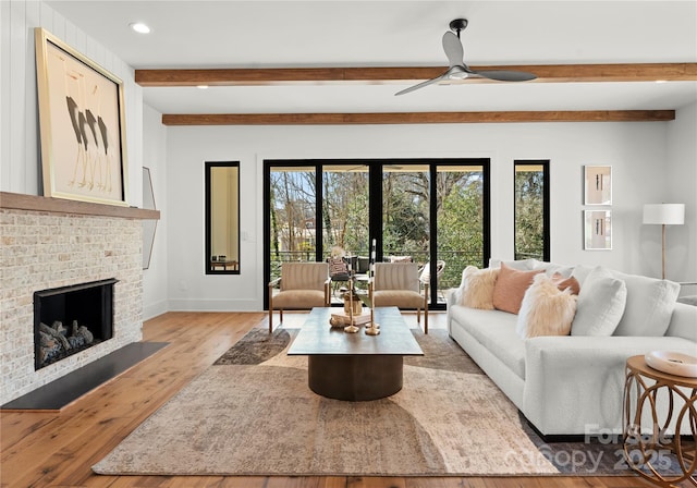 living area featuring a fireplace, beamed ceiling, light wood-style flooring, and baseboards