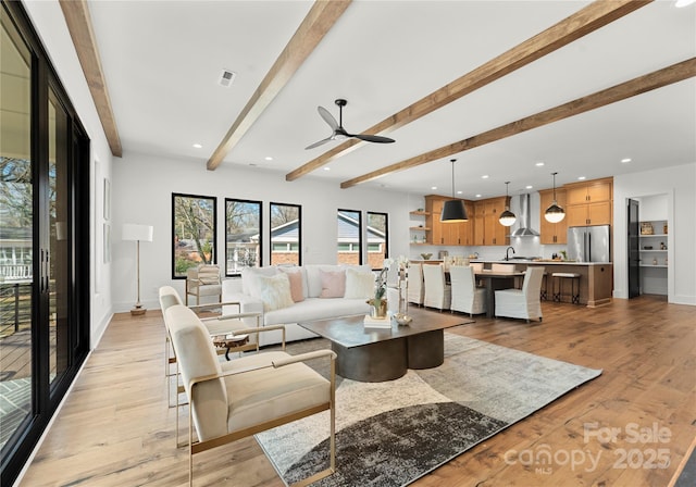 living area with light wood-type flooring, visible vents, beamed ceiling, and baseboards