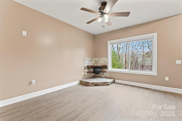 unfurnished room with hardwood / wood-style floors, ceiling fan, and a wood stove