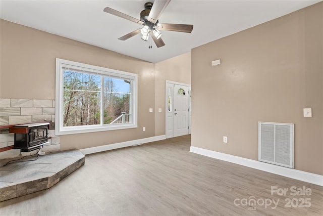 living area featuring wood-type flooring, a wood stove, and ceiling fan