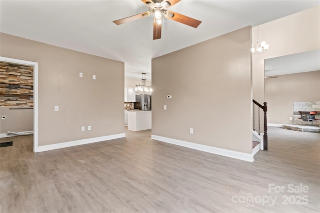 unfurnished living room with ceiling fan with notable chandelier and light hardwood / wood-style floors