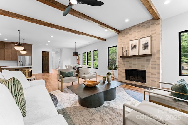 living area with recessed lighting, light wood-style flooring, a tile fireplace, beamed ceiling, and baseboards