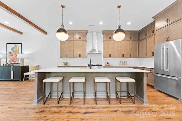 kitchen with light countertops, wall chimney range hood, high quality fridge, and a kitchen breakfast bar