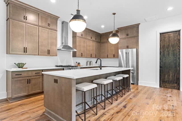 kitchen with an island with sink, light wood-style flooring, wall chimney exhaust hood, a breakfast bar area, and high end refrigerator