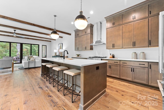 kitchen with wall chimney range hood, open floor plan, light countertops, a breakfast bar area, and light wood finished floors