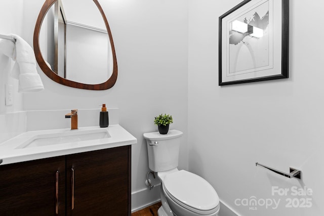 half bathroom featuring toilet, vanity, and baseboards