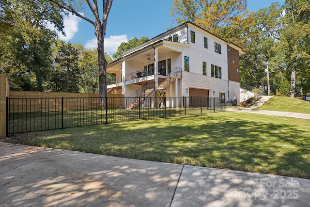 exterior space featuring stairway, a ceiling fan, an attached garage, a fenced front yard, and a lawn