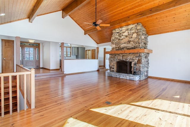 unfurnished living room with baseboards, beam ceiling, light wood-style flooring, high vaulted ceiling, and a stone fireplace