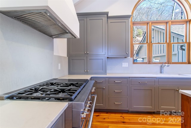 kitchen featuring stainless steel range oven, light countertops, custom exhaust hood, gray cabinetry, and a sink