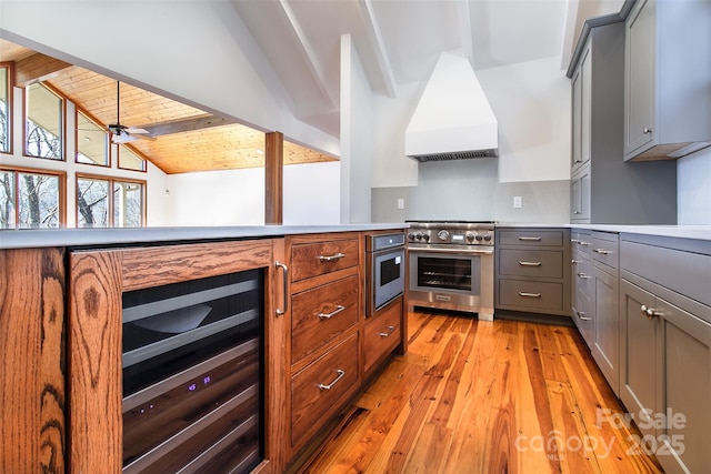 kitchen featuring premium range hood, beverage cooler, high end stove, light countertops, and vaulted ceiling with beams