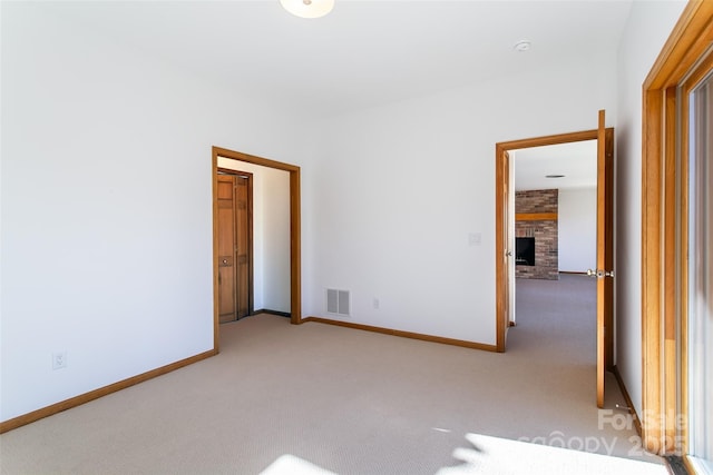 spare room with a fireplace, light carpet, baseboards, and visible vents