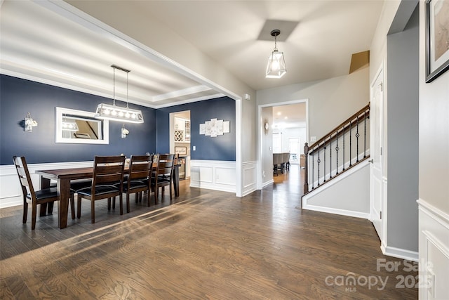 dining room with a raised ceiling, a wainscoted wall, dark wood-style flooring, stairs, and a decorative wall