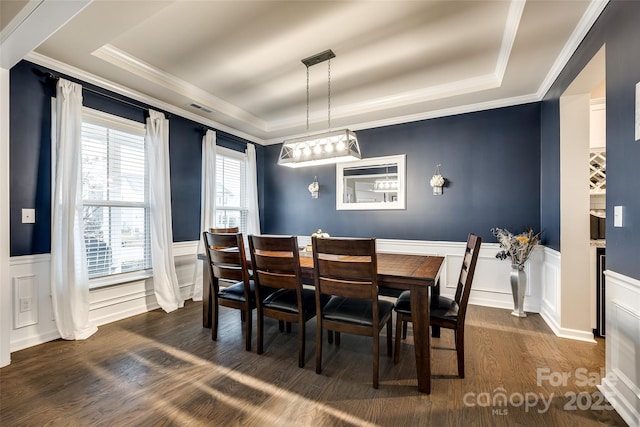 dining area with a tray ceiling, dark wood-style flooring, visible vents, ornamental molding, and wainscoting