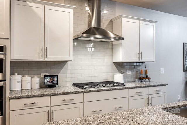 kitchen featuring appliances with stainless steel finishes, white cabinetry, wall chimney range hood, and decorative backsplash