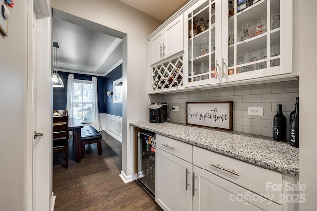 kitchen featuring light stone counters, wine cooler, glass insert cabinets, wainscoting, and white cabinets