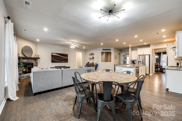 dining area with dark wood finished floors, recessed lighting, visible vents, a ceiling fan, and a stone fireplace