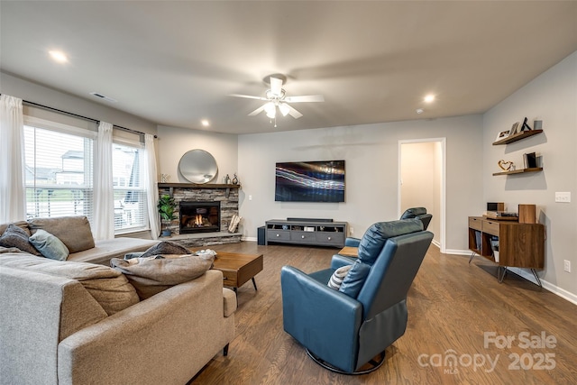 living room with visible vents, a stone fireplace, baseboards, and wood finished floors