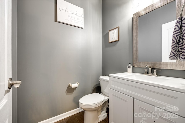 half bathroom with baseboards, vanity, toilet, and wood finished floors