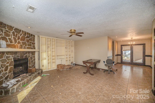 unfurnished living room with ceiling fan with notable chandelier, tile patterned flooring, a stone fireplace, and a textured ceiling