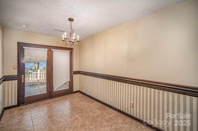 tiled empty room featuring a chandelier and a textured ceiling