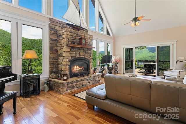 living area with high vaulted ceiling, a fireplace, ceiling fan, and wood finished floors